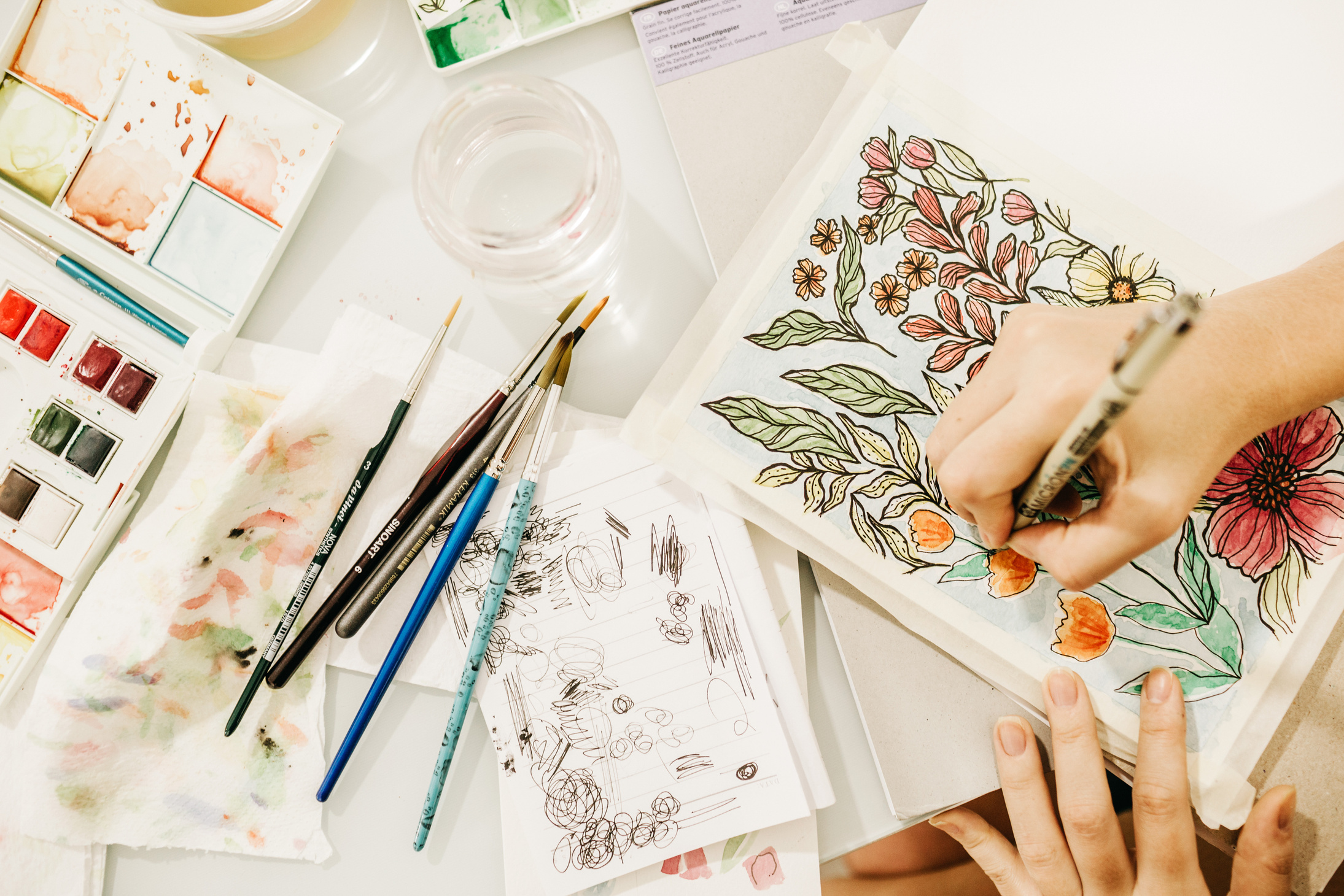 Crop artist painting flowers in sketchbook